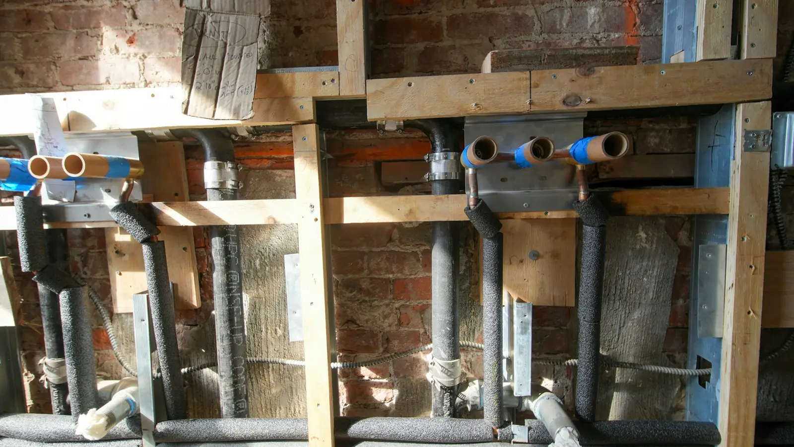 Open wand met nieuw aangelegde water- en afvoerleidingen tussen houten regels